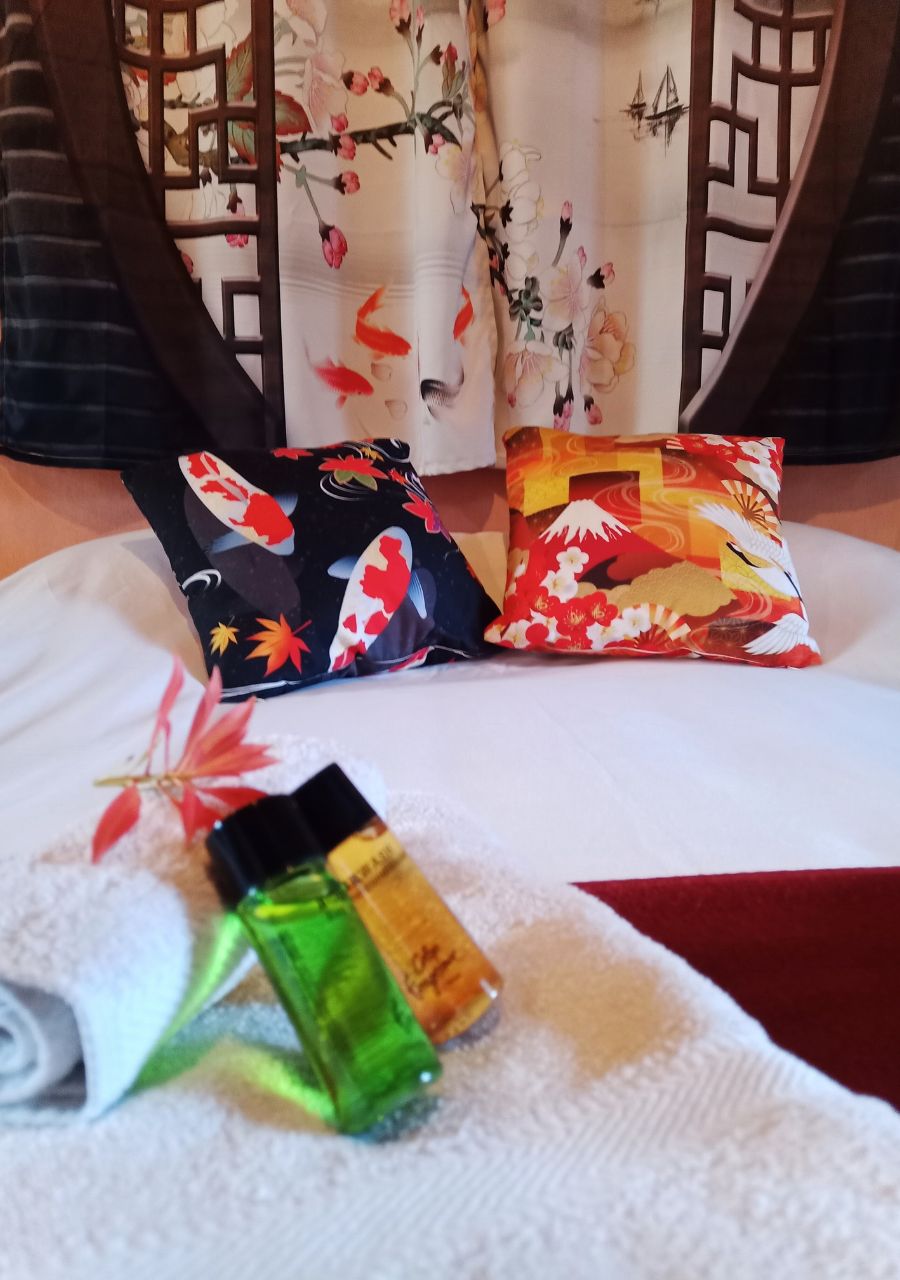 Een bed met een witte spreidek, twee sierkussens met bloemenmotieven en twee kleine flesjes op het bed.