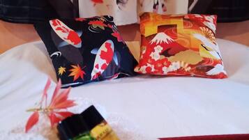 Een bed met een witte spreidek, twee sierkussens met bloemenmotieven en twee kleine flesjes op het bed.