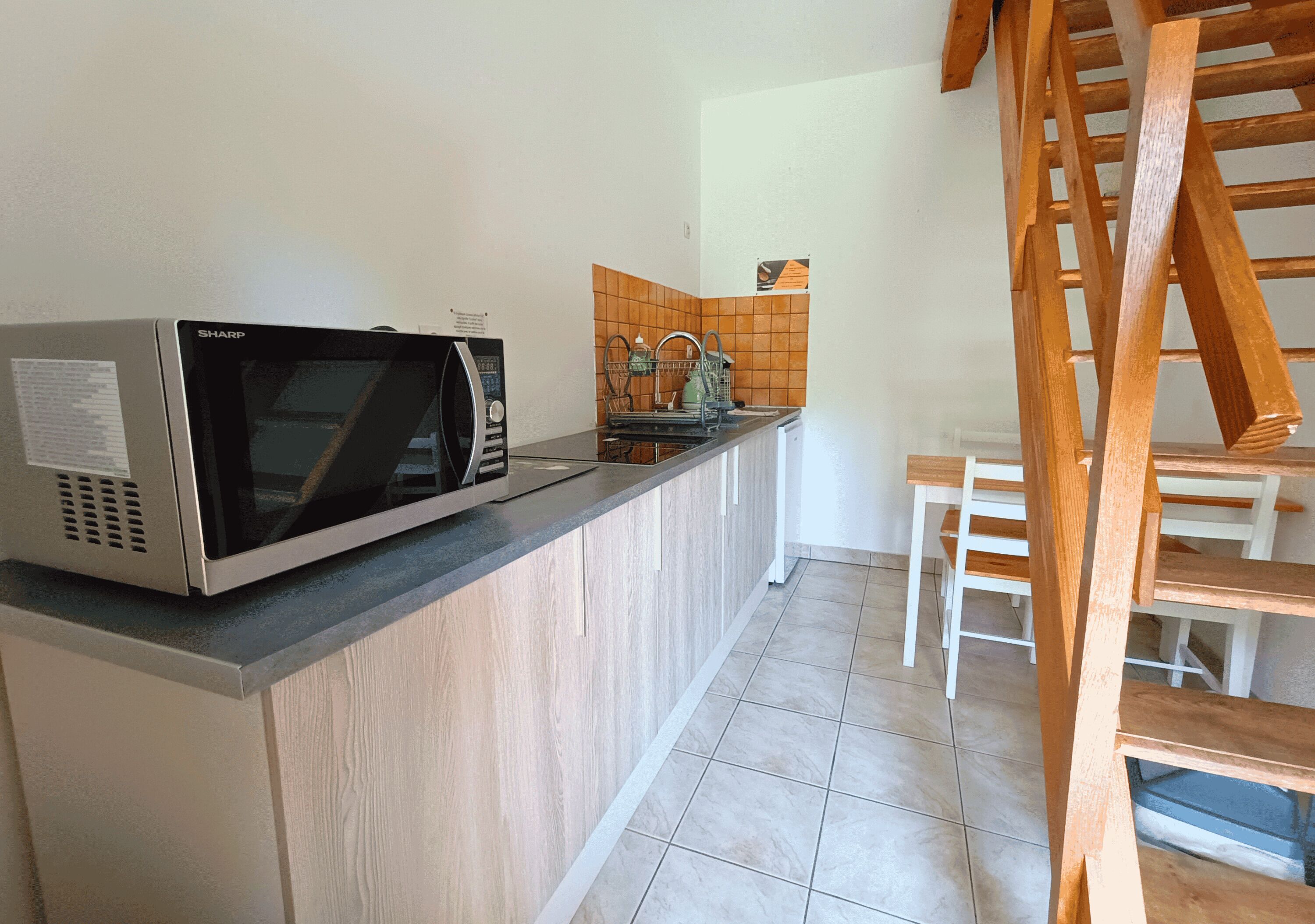 Una cocina con microondas, un lavamanos y una escalera de madera.