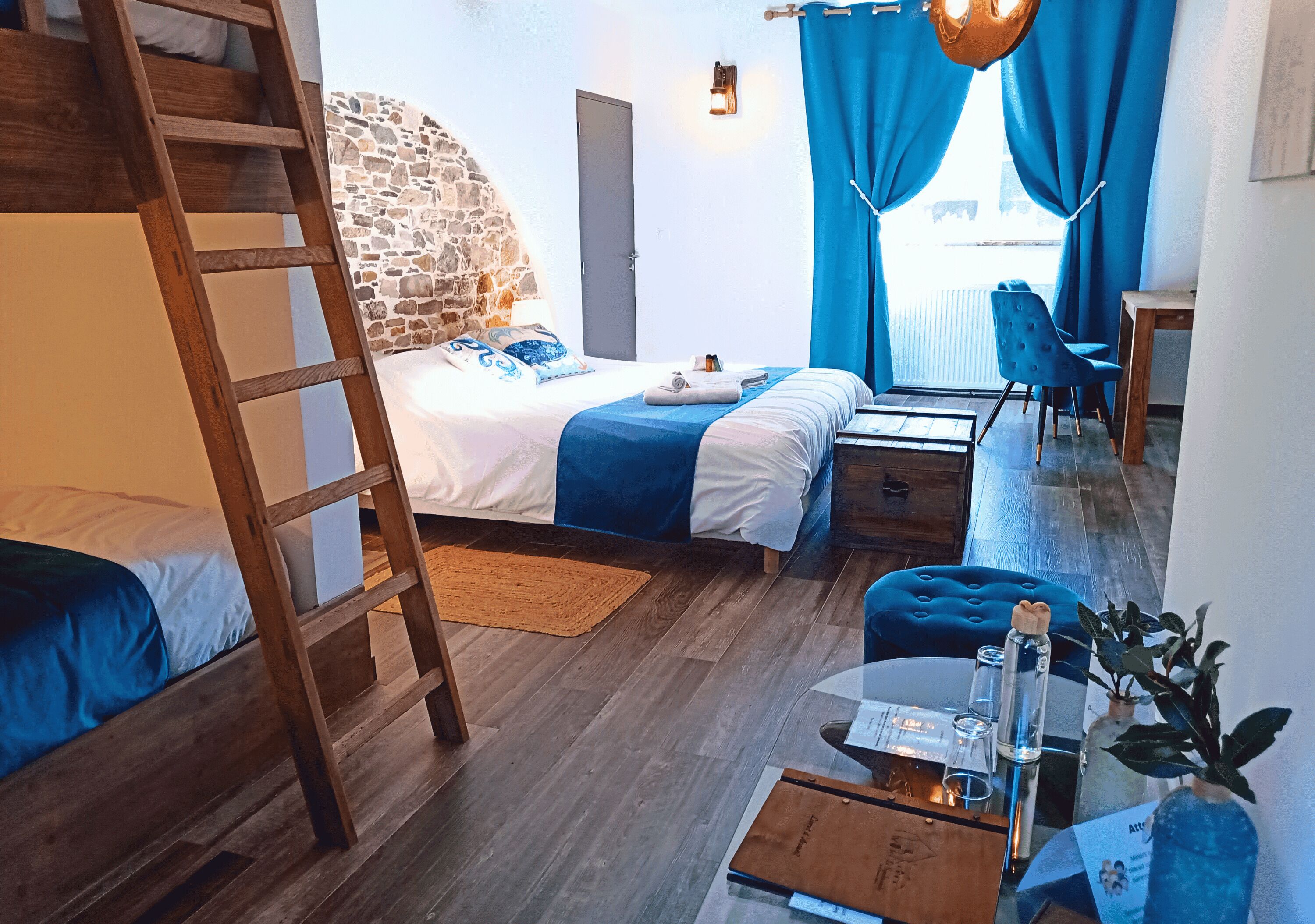 Un dormitorio con literas, un escritorio, una silla, una escalera y una pared de piedra, además de vistas al exterior.