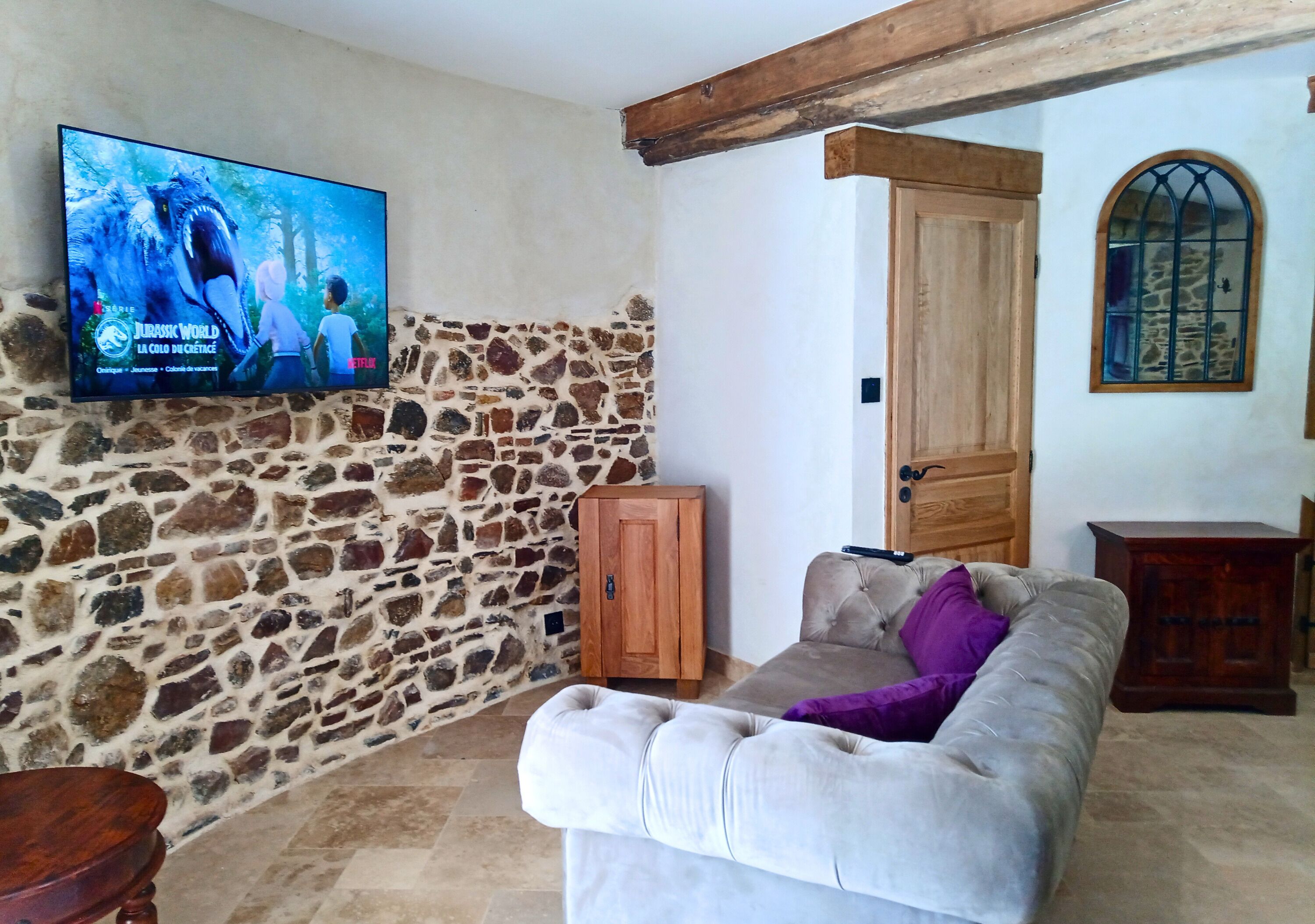 Una sala de estar con pared de piedra, televisor, puerta de madera y sofá acolchado.