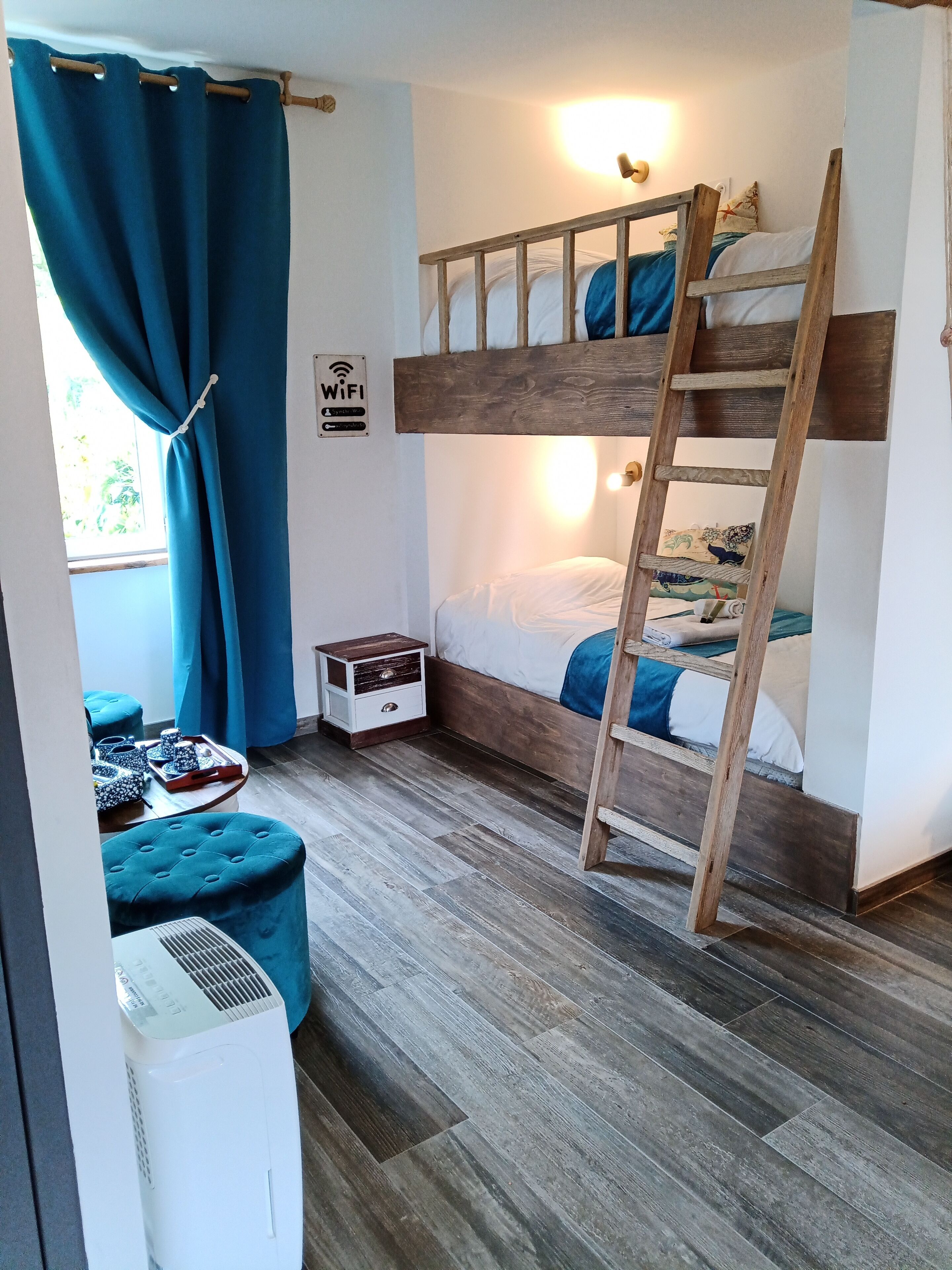 Une chambre avec un lit superposé, une échelle en bois, une petite table de chevet et un panneau indiquant la présence d’une prise de courant.