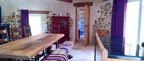 A rustic dining area with a wooden table and benches, stone walls, and a view through a glass railing.