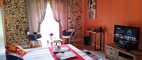 Quarto de hotel com cama, televisão, escrivaninha e parede de pedra.