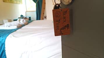 Una cama bien hecha con una manta azul y un llavero de madera con la inscripción 'BLACK PEARL' colgado en la pared.