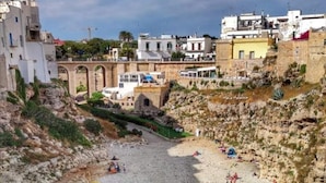 Eine Küstenstadt mit Kiesstrand, klarem, blauem Wasser und Gebäuden im Hintergrund.