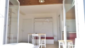 Ein Zimmer mit weißem Tisch, zwei Hocker, einer Bank und einer Schiebetür.