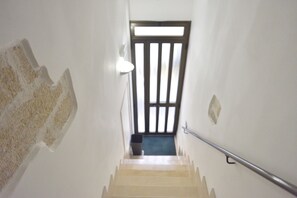 Una escalera con barandilla, una puerta con listones verticales y una lámpara en la pared.