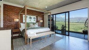 A modern bedroom with a four-poster bed, a large window with a view of the countryside, and a balcony with outdoor seating. - Dragonview Lodge (Cathkin Park)