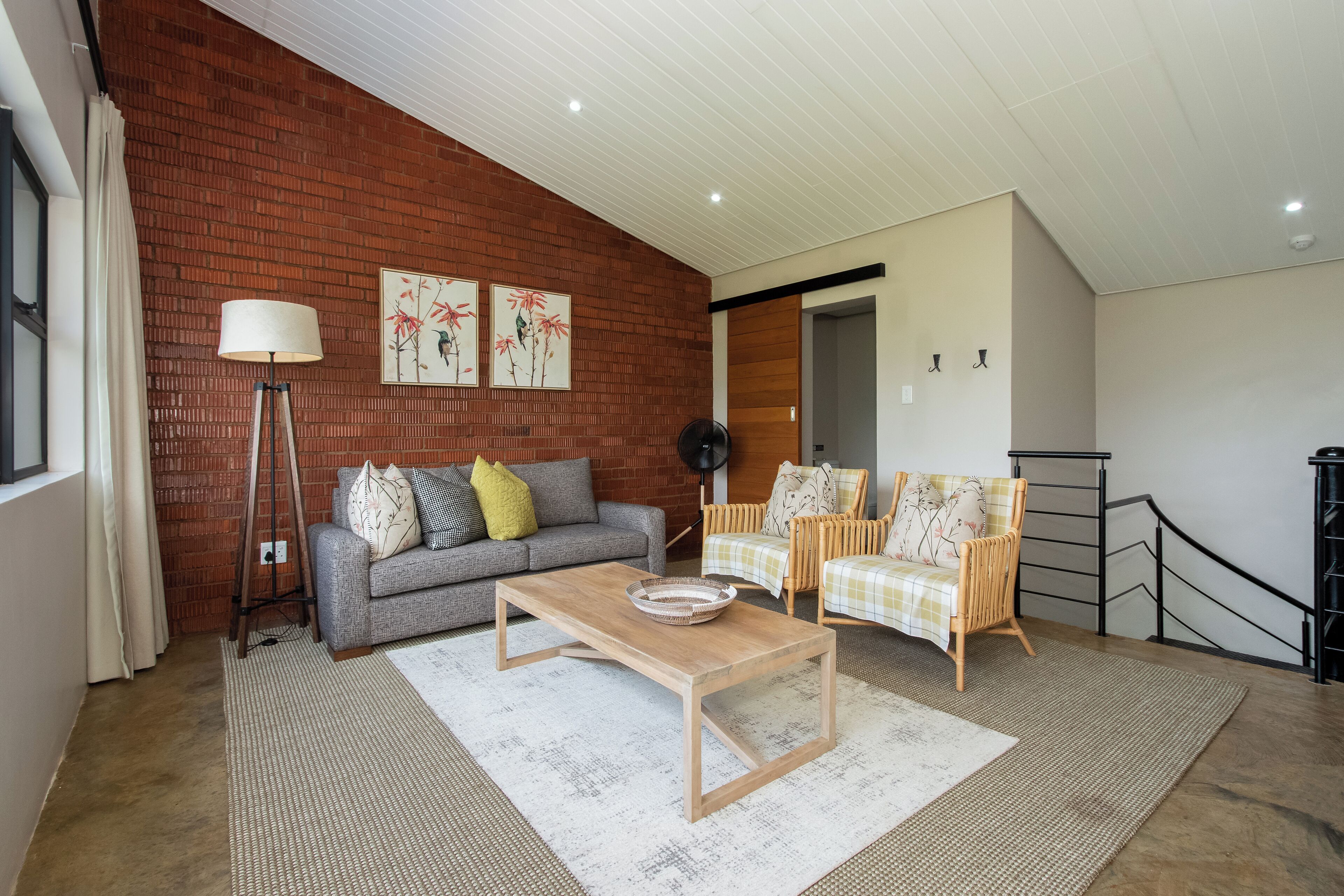 A living room with a brick wall, a grey sofa, a wooden coffee table, and two wicker chairs.