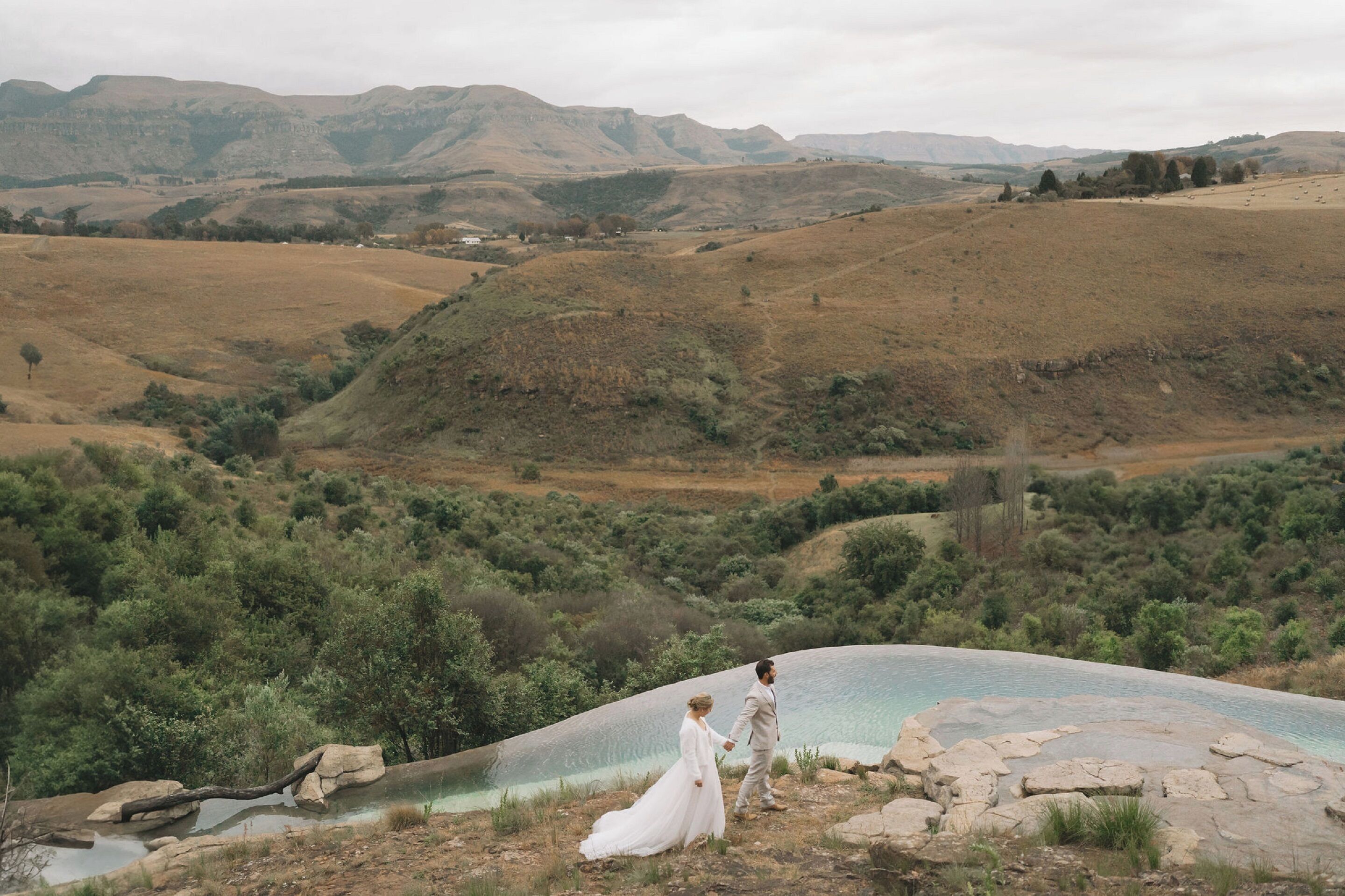 Una pareja parada junto a una piscina natural rodeada de colinas y vegetación.