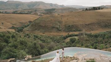 Una pareja parada junto a una piscina natural rodeada de colinas y vegetación.