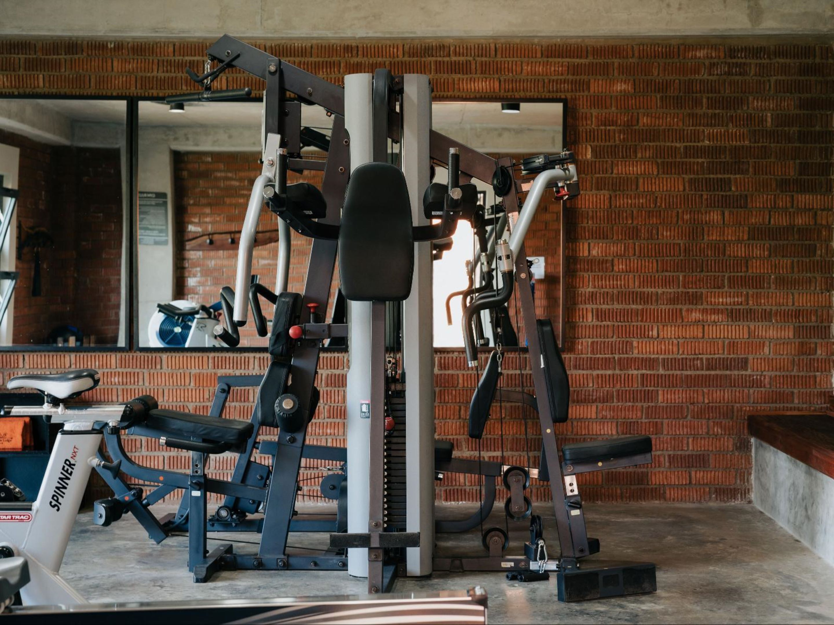 Un gimnasio con diversos equipos de ejercicio, una pared de ladrillo y un espejo grande.