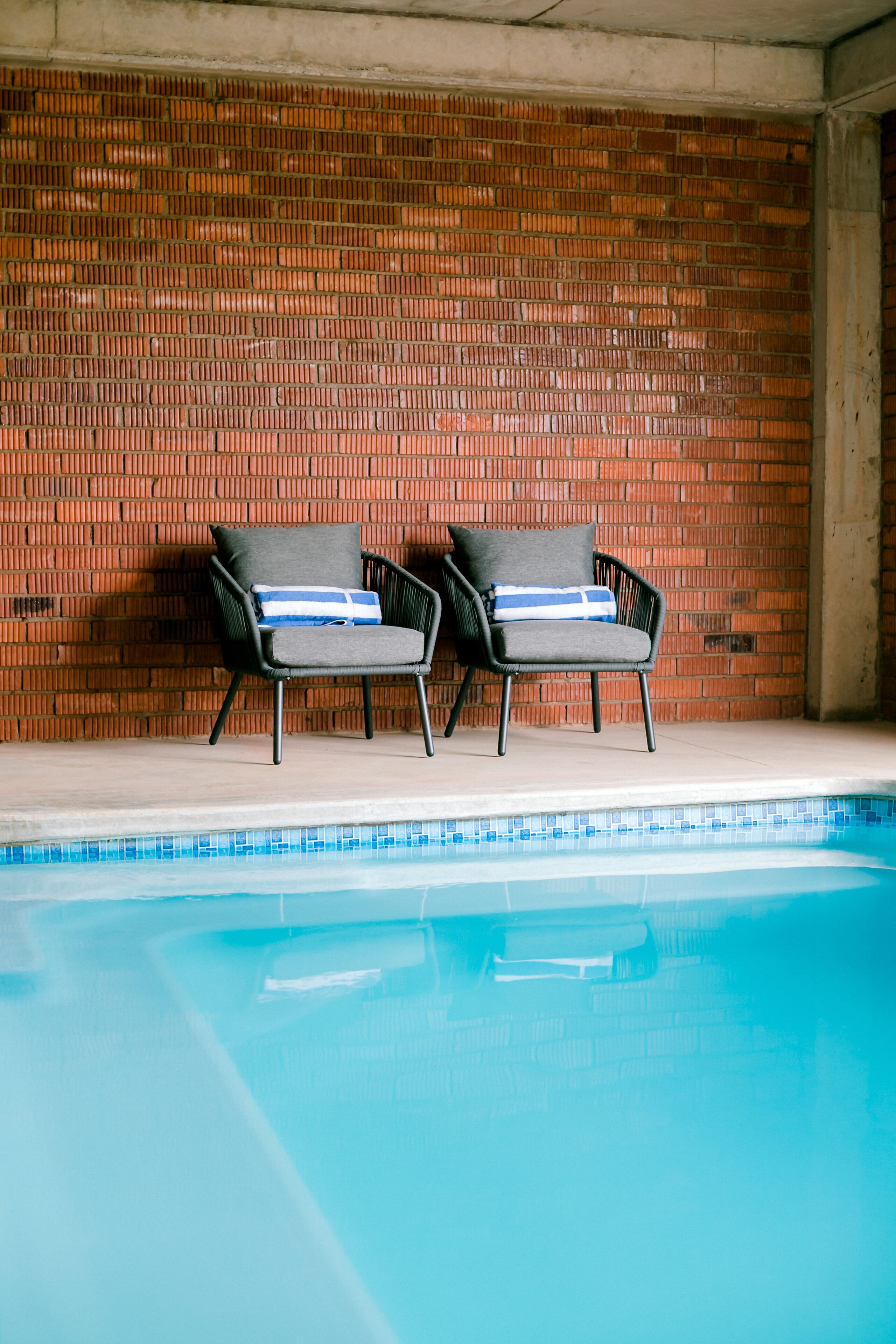 Un espace aménagé au bord de la piscine, avec deux chaises longues et un mur en briques.