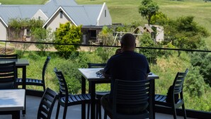 A man seated at a table with a view of green hills and a mountain range in the distance. - Dragonview Lodge (Cathkin Park)