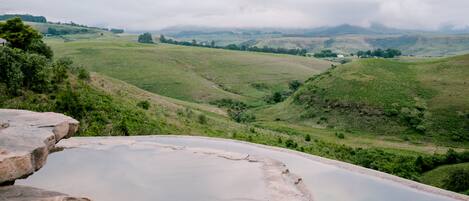 Une vue panoramique d’une vallée avec une vaste étendue d’eau calme, entourée de collines verdoyantes et surplombée par un ciel nuageux.