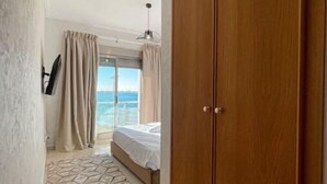 Ein Hotelzimmer mit großem Holzschrank, einem Bett mit Meerblick und einem gemusterten Teppich.