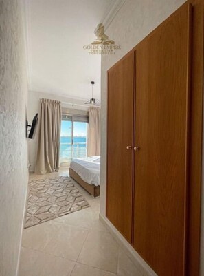 A hotel room with a large wooden wardrobe, a bed with a view of the sea, and a patterned rug on the floor. - Océan Vue 2 (Tanger)