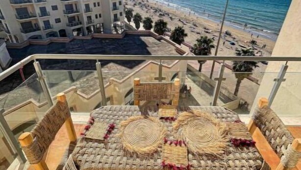 Ein Balkon mit Tisch und Stühlen mit Blick auf einen Strand und den Ozean.
