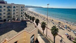 Ein Strand mit blauem Himmel, Sonne und einem Gebäude mit Balkonen, das auf den Strand blickt.
