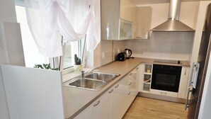 A modern kitchen with white cabinets, stainless steel appliances, and a wooden floor.