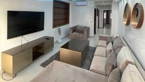 A modern living room with a flat-screen TV, a sofa, a coffee table, and a wall-mounted TV.