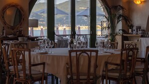 Un comedor con mesas dispuestas para dos, ventanas amplias con sombrillas y vista al mar.