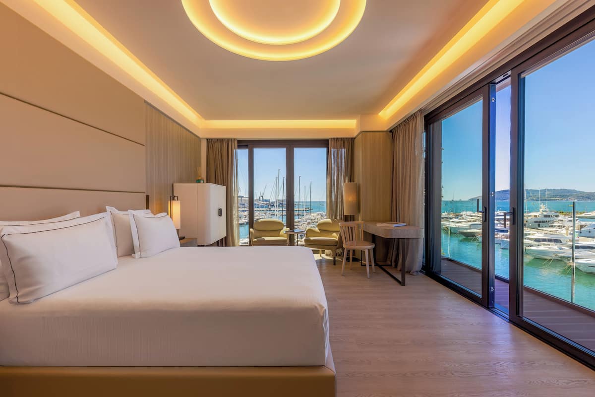 A hotel room with a large bed, a desk, and a view of the marina.