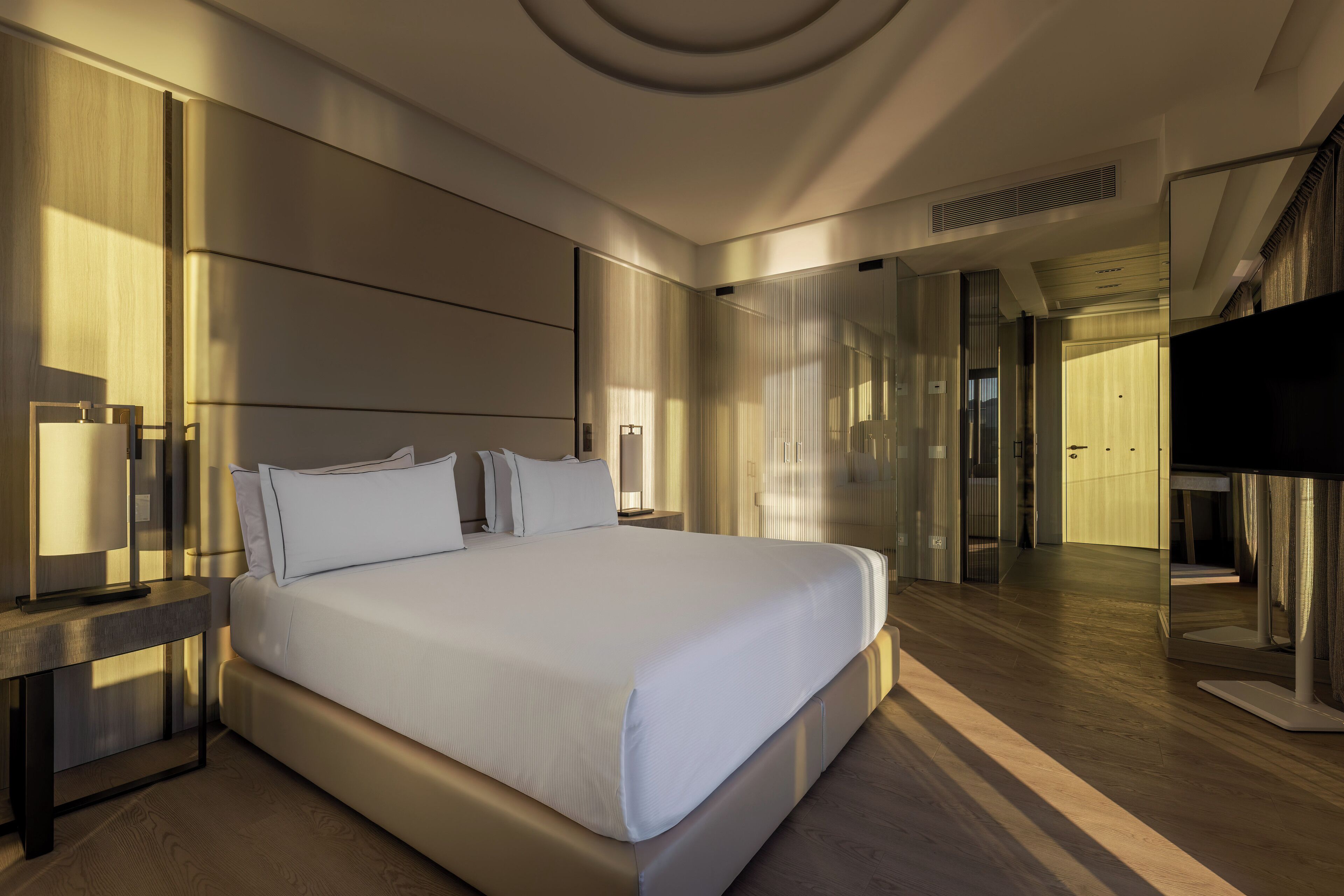 Une chambre d’hôtel moderne dotée d’un grand lit, de tables de chevet, d’un téléviseur à écran plat et d’un miroir.