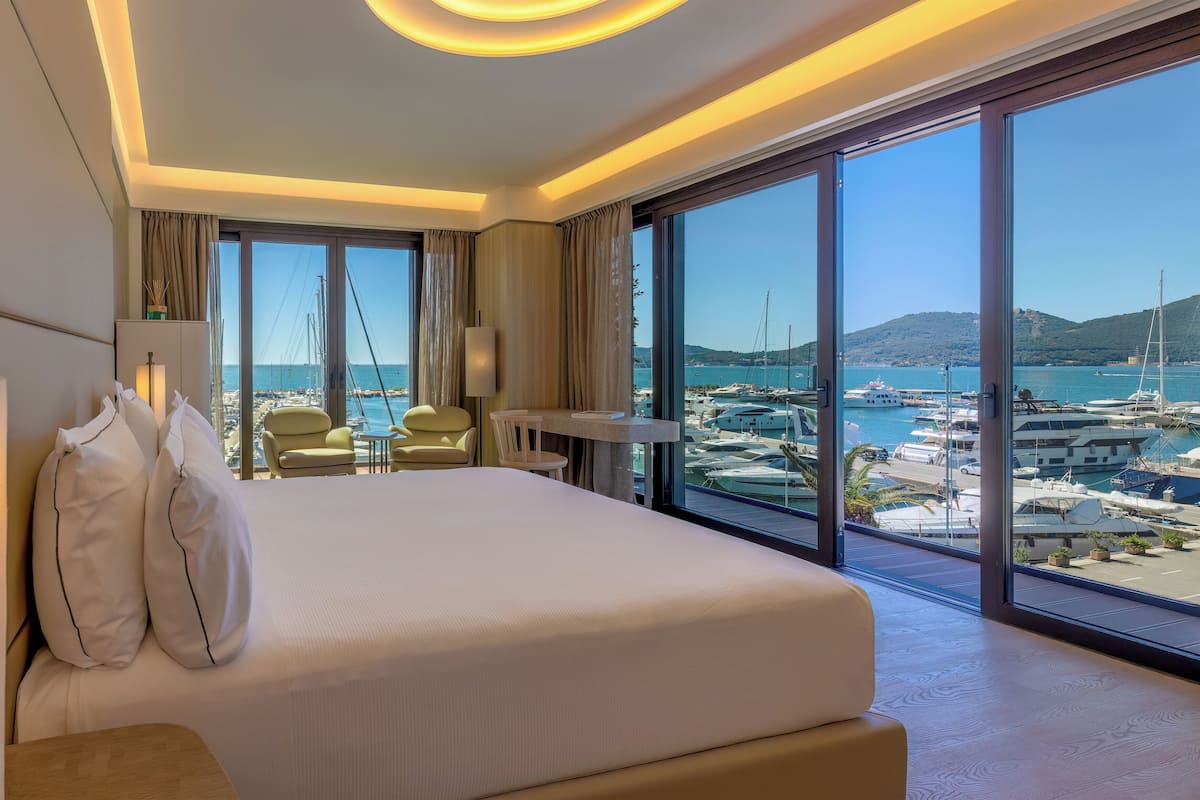 A hotel room with a large bed, a desk, and a view of a marina.