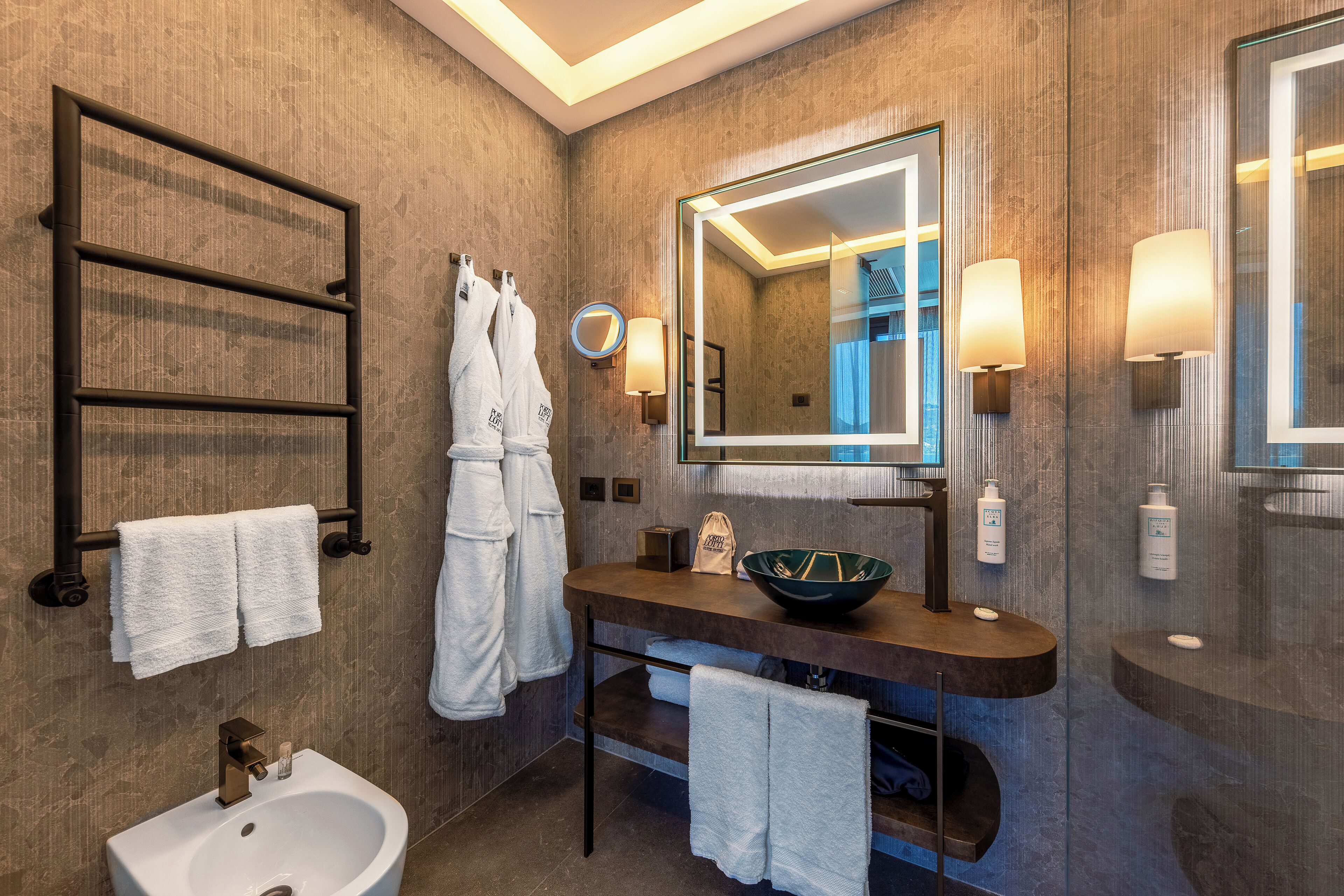 A modern bathroom with a large mirror, a sink, a bidet, and towel racks.