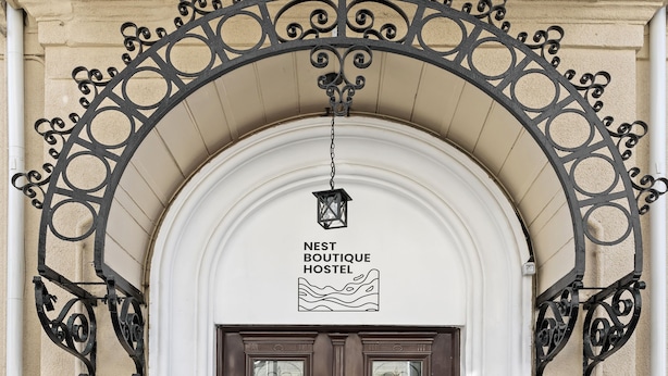 A hotel entrance with a decorative metal archway, a sign above the door, and a small trash bin to the left. - Nest Boutique Hostel (Bucharest)