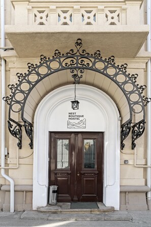 A hotel entrance with a decorative metal archway, a sign above the door, and a small trash bin to the left. - Nest Boutique Hostel (Bucharest)