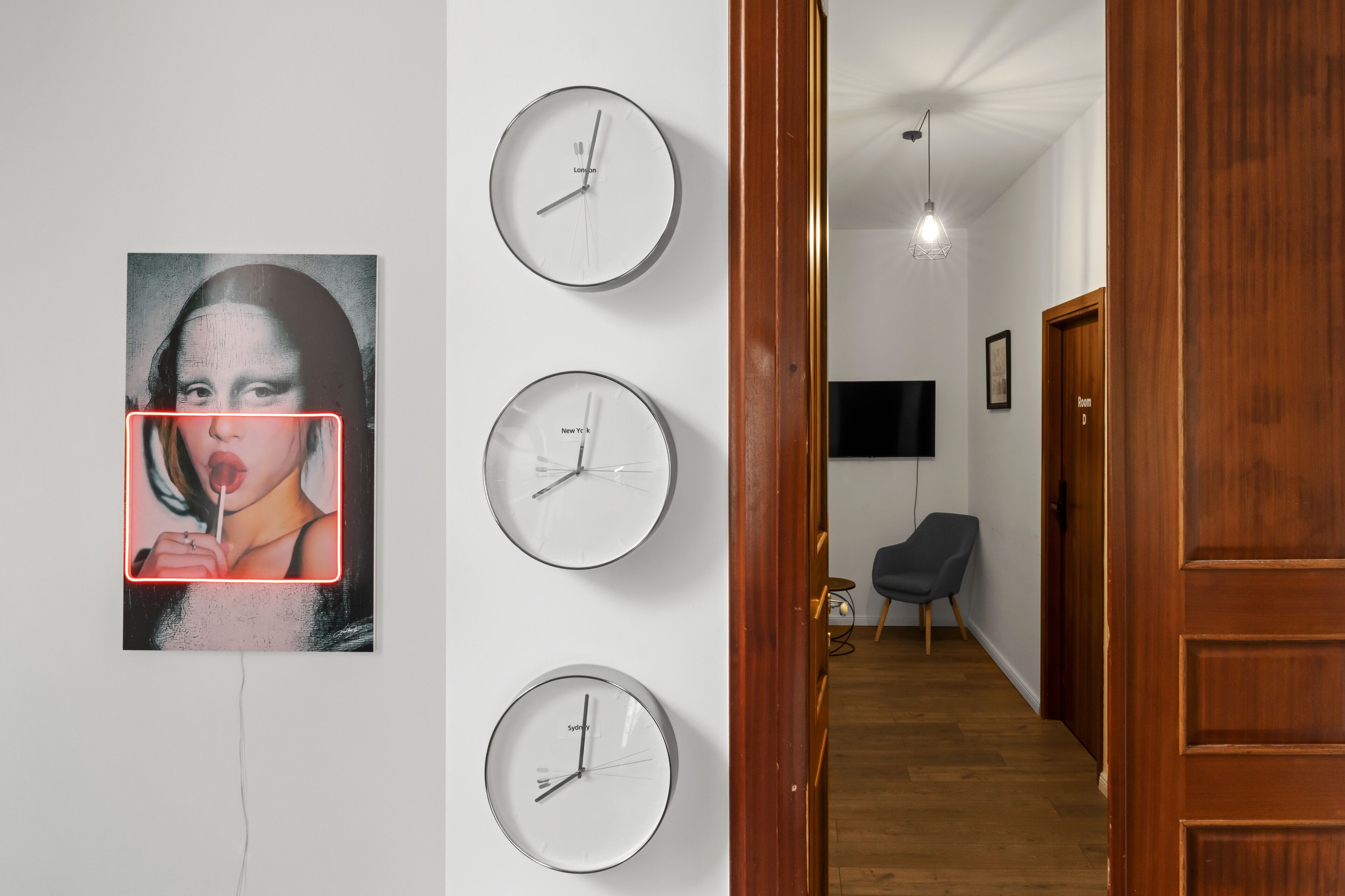 Un pasillo con una puerta de madera, una silla negra y un televisor montado en la pared.