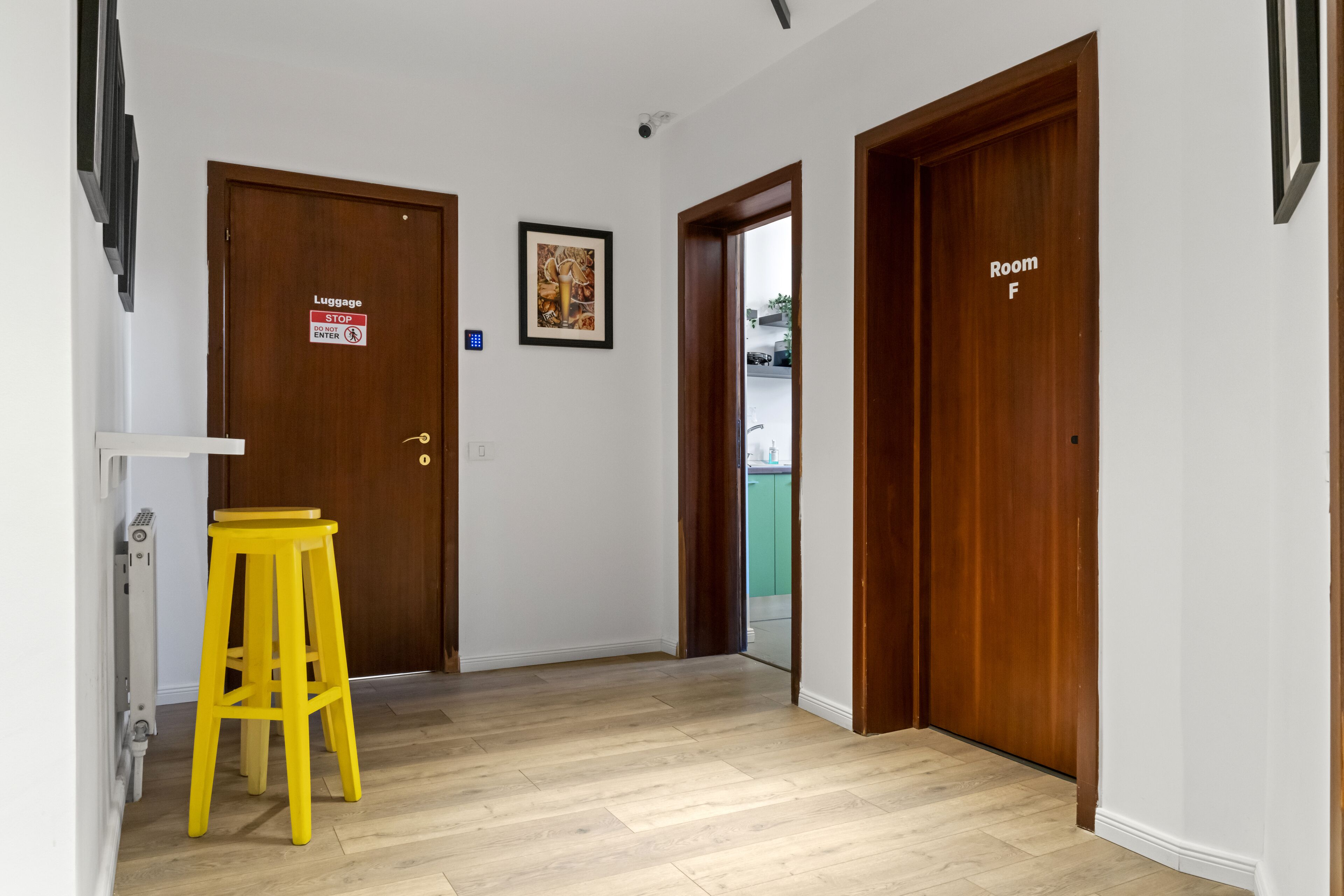 A hallway with two wooden doors, one labeled "Luggage STOP" and the other "Room F". A yellow stool is placed against the wall near the doors.
