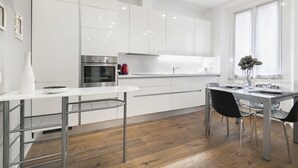 Eine moderne Küche mit weißen Schränken, einem Edelstahlbackofen und einer Essecke mit Tisch und Stühlen.