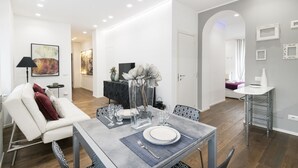 Ein modernes Wohnzimmer mit Essbereich, mit einem weißen Sofa, einem Esstisch gedeckt mit Tellern und Gläsern, und einer Vase mit Blumen.
