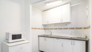A compact kitchen with white cabinets, a microwave, a sink, and a coffee storage container. - Estudio Encantador Plaza España (Madrid)