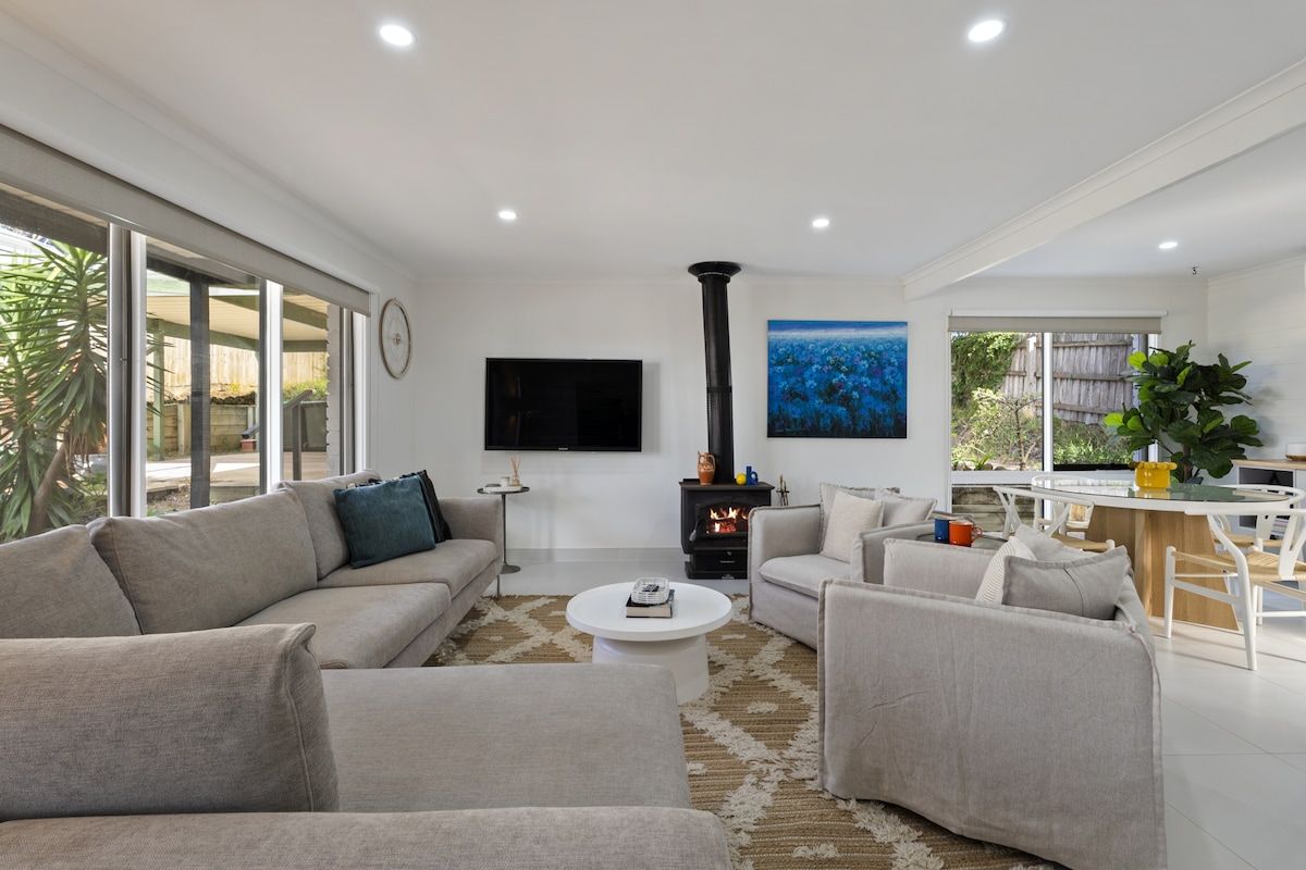 A modern living room with a fireplace, sofas, a coffee table, and a TV mounted on the wall.