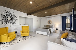 Un dormitorio moderno con una cama, dos sillones amarillos, un sofá blanco y una alfombra geométrica.