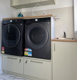 A compact kitchen with two front-loading washers, a sink, and a cabinet with drawers.