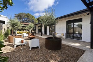 An outdoor seating area with white chairs and a fire pit, surrounded by gravel and potted plants.