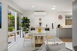 A modern kitchen with a glass dining table, white cabinetry, and a large window.
