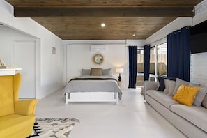 Un dormitorio con cama, sofá, techo de madera y ventana con cortinas.