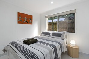 A bedroom with a bed, a window, a bedside lamp, and a painting on the wall.
