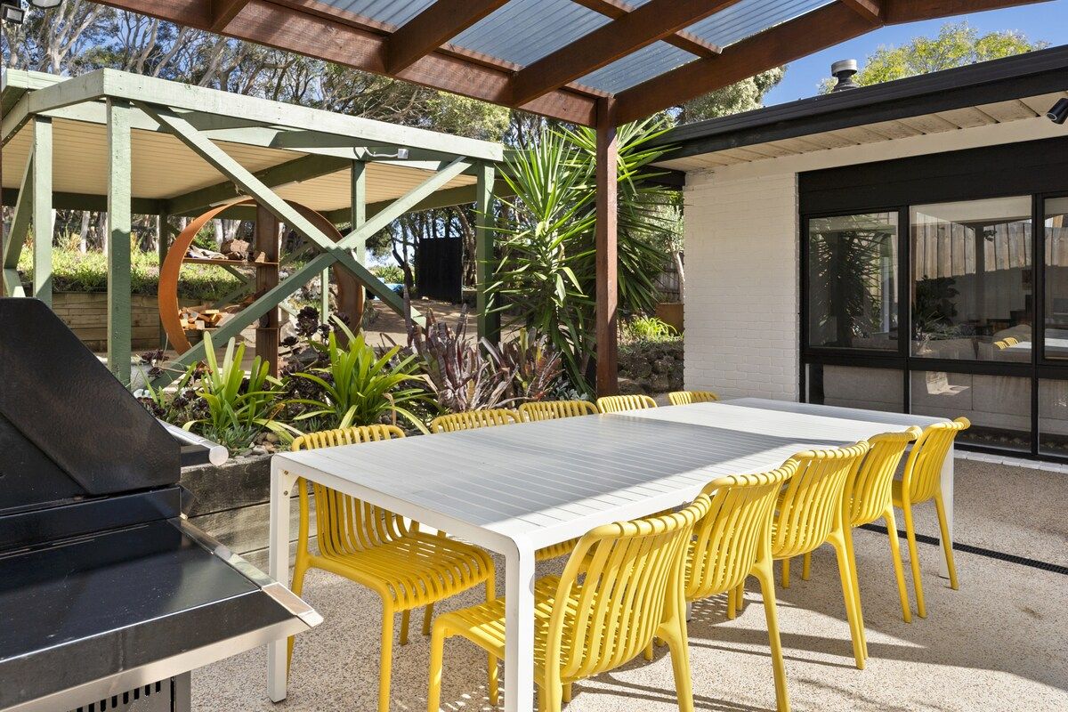 Une terrasse extérieure avec un barbecue, des chaises jaunes et une table.