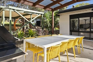Un patio exterior con una parrilla, sillas amarillas y una mesa.