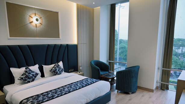 A modern hotel room with a large bed, a seating area with a table, and a view of the outdoors. - Hotel Casa Royal (Amritsar)