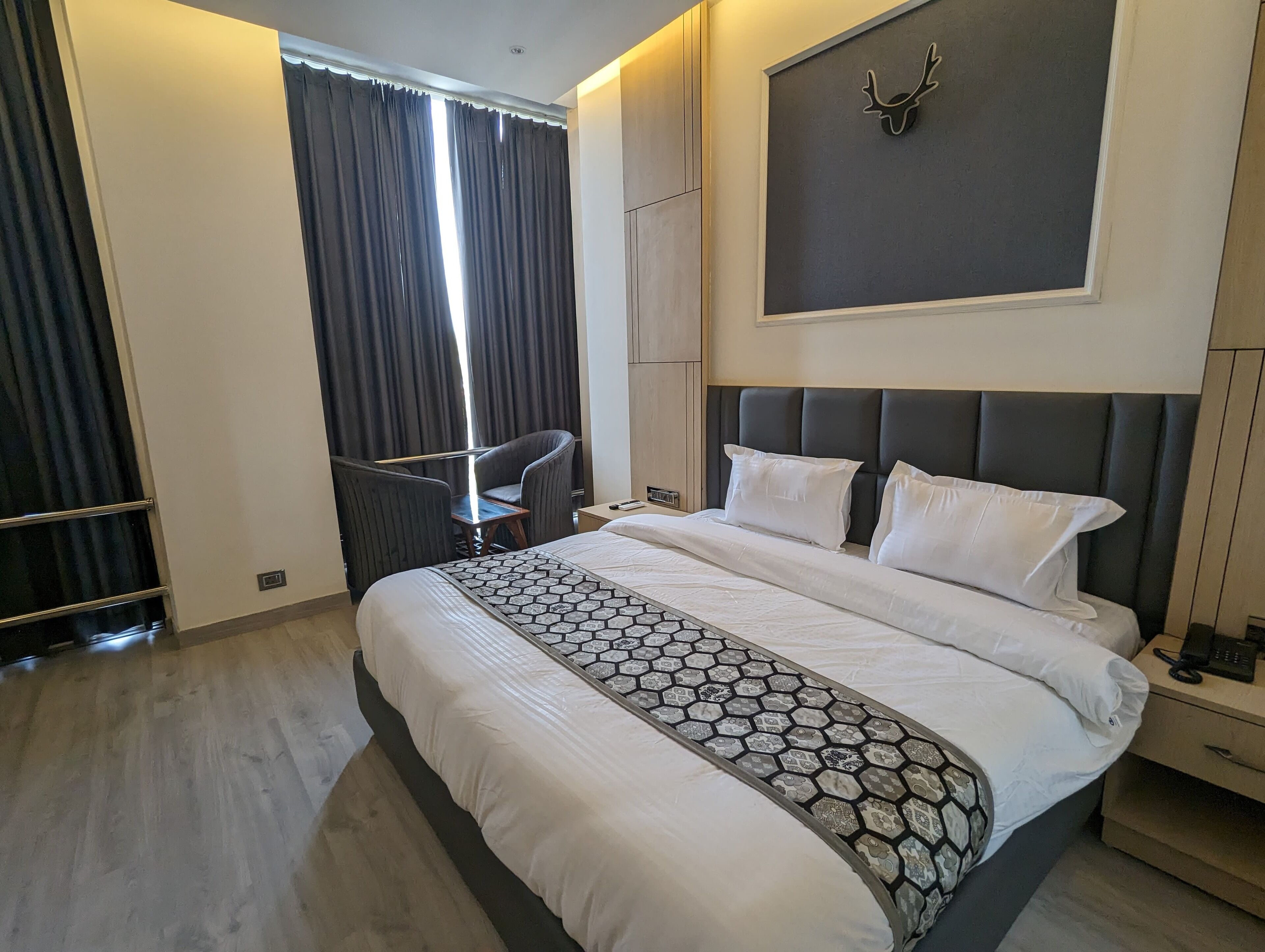 A hotel room with a large bed, a chair, a desk, and a wall-mounted deer head decoration.