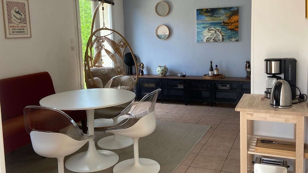 A modern kitchen with a dining area, featuring a round table with four chairs, a hanging chair, and a coffee machine.